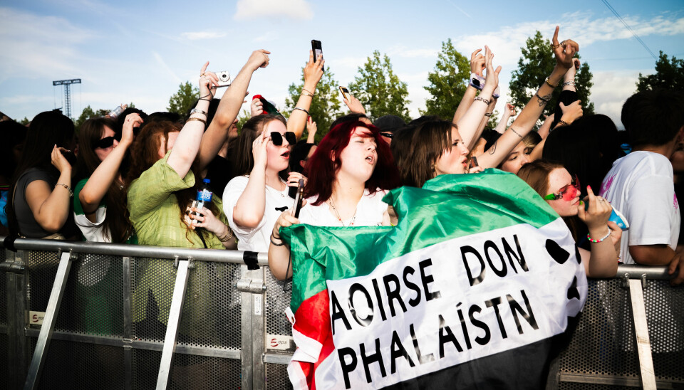 Fans holding up a Palestinian flag saying “Freedom for Palestin” in irish at a Kneecap concert in London. A crowd of people on a concert. In the middle there is a person holding up a palestininan flag saying 'Saoirse don Phalaistn' which means 'Freedom for Palestin' in irish.