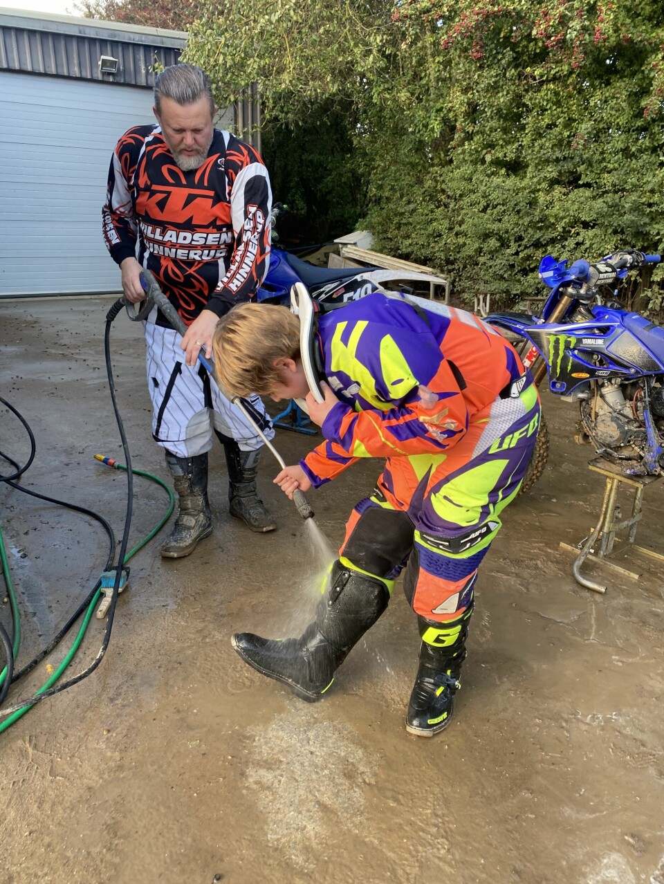 Far og søn hjælper hinanden med at vaske mudder af både cykel og støvler