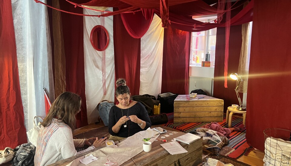 To kvinder broderer motiver. De sidder i rummet 'living womb', som skal forestille en livmor, til festivalen Den Nye By.