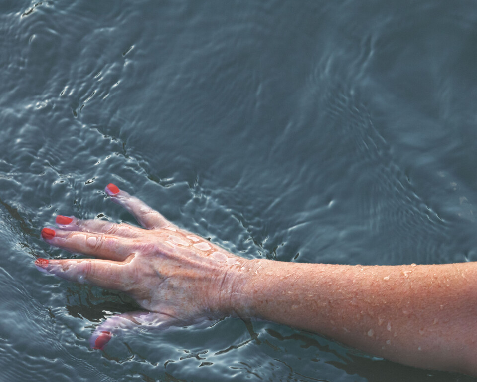 womans hand with red painted fingernails touching the wavy water