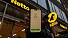 A man is standing in front of a netto supermarket holding his phone with thge 'udenUSA' app open.
