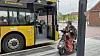Gitte Kate Jensen sidder på sin el-scooter foran en gul bus. Hun kigger til sin højre side, for at tale med buschaufføren, der sidder inde i bussen.