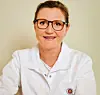 Portræt af en kvinde i hvid kittel med briller, fotograferet mod en lys baggrund.