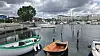 Small boats in a harbor with a tree and buildings under grey clouds.