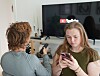 En ung kvinde ser på sin smartphone, mens en anden person sidder foran et fjernsyn med YouTube-logoet.