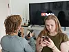 En ung kvinde ser på sin smartphone, mens en anden person sidder foran et fjernsyn med YouTube-logoet.