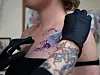 Gloved tattoo artist positions a stencil on a client’s upper chest.