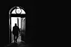 Silhouetted night courier exits an arched residential doorway in Aarhus.