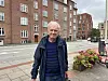 Ældre mand i mørkt tøj står på et fortov foran røde murstenshuse.