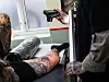 A tattoo artist photographs an intricate finished tattoo on a client’s lower leg in a studio.